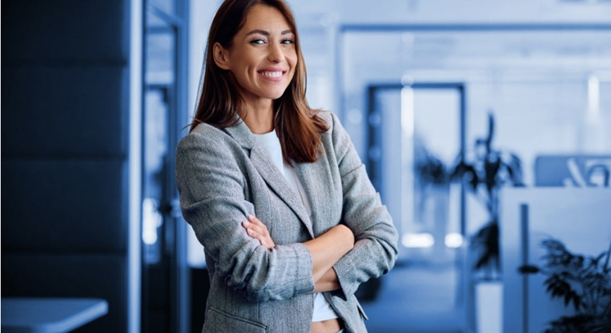 Woman in an office wearing business suit and smiling with arms crossed
